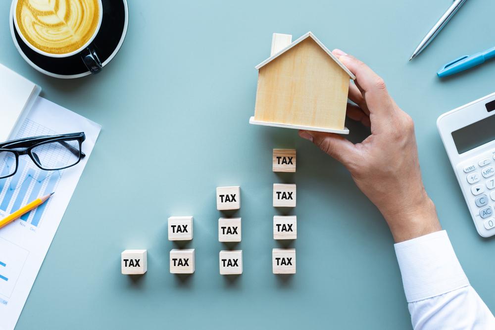 Image of man holding small wooden house over blocks with tax written on them
