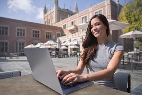Woman working on a computer outside on a patio surrounded by a building