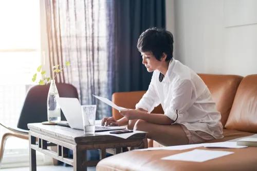 Picture of woman looking at a piece of paper and scrolling on her computer